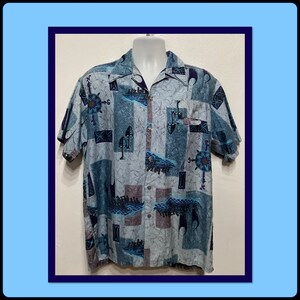Può includere: Una camicia a maniche corte con bottoni di colore blu e grigio con un motivo geometrico. Il motivo presenta forme astratte, onde e un design a bussola.