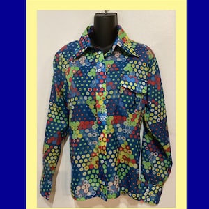 May include: A long-sleeved button-down shirt with a vibrant, retro design. The shirt features a dark blue background covered in colorful polka dots in shades of red, yellow, green, and blue. It has a collared neckline and a single chest pocket.