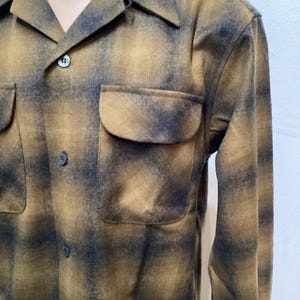 以下が含まれることがあります： 茶色と黒の色合いのチェック柄の長袖シャツ。胸に2つのポケットとクラシックな襟が付いています。生地は中程度の厚さのようです。 シャツはボタンで留められています。