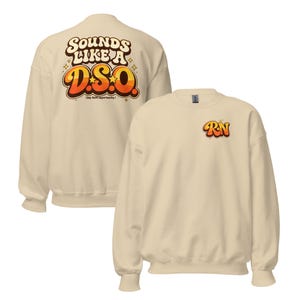 Op de afbeelding: Een crèmekleurige sweatshirt met de tekst "SOUNDS LIKE A D.S.O." in een retro lettertype op de rug en "RN" op de voorkant. Het ontwerp heeft oranje en gele gradiëntletters met steraccenten en de zin "(my shift opportunity?)" onder de hoofdtekst.