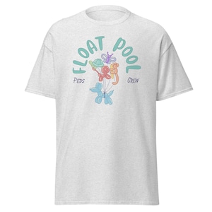 Könnte beinhalten: Ein hellgraues T-Shirt mit dem Text "FLOAT POOL CREW" in Türkis, mit einer Grafik von Ballon-Tieren. Zu den Ballon-Tieren gehören eine Schildkröte, ein Schmetterling, ein Affe und ein Hund.