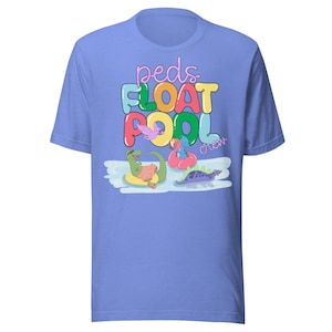 May include: A light blue t-shirt featuring the text "peds FLOAT POOL crew" in colorful bubble letters. The graphic includes cartoon dinosaurs in inflatable rings, floating in water. The design is playful and whimsical.