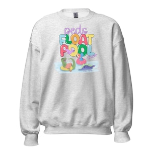 Könnte beinhalten: Ein graues Sweatshirt mit dem Text "Peds Float Pool" in bunten Buchstaben. Der Text ist von Cartoon-Dinosauriern umgeben, die auf Pool-Schwimmringen treiben.