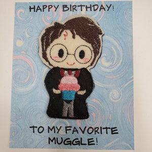 Op de afbeelding: Een verjaardagskaart met een blauwe achtergrond en een cartoonafbeelding van Harry Potter die een cupcake vasthoudt. De kaart zegt "Happy Birthday! To my favorite Muggle!"