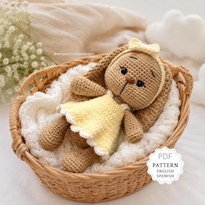 Puede incluir: Muñeca de conejo de ganchillo con orejas largas, vestida con un vestido amarillo y una diadema a juego con lazo. Descansa en una cesta de mimbre sobre una manta blanca. El texto "PDF PATTERN ENGLISH SPANISH" está incluido.