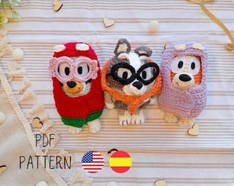 May include: Three crocheted stuffed animals wearing glasses. The animals are a red and green dog, a gray and orange dog, and a purple dog. The image includes the text "PDF PATTERN" and flags for the United States and Spain.