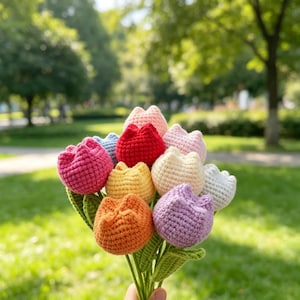 Könnte beinhalten: Ein Strauß aus gehäkelten Tulpen in verschiedenen Farben wie Rot, Rosa, Orange, Gelb, Lila, Weiß und Hellblau. Jede Blume hat eine abgerundete, strukturierte Blütenform, die an grünen gehäkelten Stielen und Blättern befestigt ist.