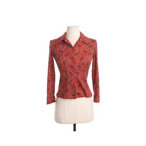 May include: Red long-sleeve shirt with a paisley pattern. The shirt has a collared neckline and is displayed on a mannequin. The paisley design includes black, green, and tan accents. The shirt is a fitted style.