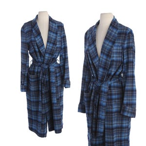 May include: A long-sleeved robe featuring a blue, black, and grey plaid pattern. The garment includes a shawl collar, a matching fabric tie belt at the waist, and two front patch pockets. The robe is displayed on a mannequin in two views.