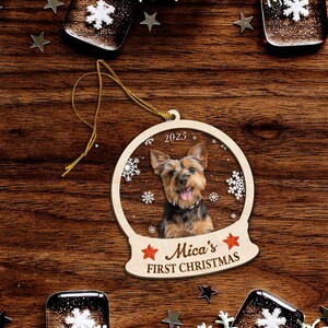 May include: A wooden Christmas ornament featuring a Yorkshire Terrier dog inside a snow globe design. The ornament has the text "Mica's FIRST CHRISTMAS" and the year "2023". The ornament is hanging by a gold string.
