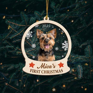 May include: A wooden Christmas ornament featuring a Yorkshire Terrier dog inside a snow globe design. The ornament has the text "2025" at the top and "Mica's FIRST CHRISTMAS" at the bottom, with red star accents. The ornament hangs from a gold string.