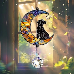 May include: A stained glass suncatcher featuring a black dog sitting on a crescent moon with a star. The suncatcher is hanging from a window and has a crystal prism hanging from the bottom.
