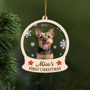 May include: Wooden Christmas ornament featuring a Yorkshire Terrier dog inside a snow globe design. The ornament includes the text "2025" and "Mica's FIRST CHRISTMAS" with snowflake and star accents. A gold string is attached for hanging.