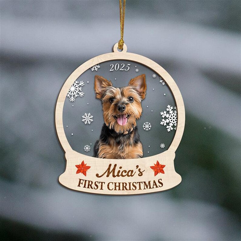 May include: Wooden Christmas ornament featuring a Yorkshire Terrier inside a snow globe design. The ornament includes the text "2025" at the top and "Mica's FIRST CHRISTMAS" at the bottom, with red star accents. The dog has brown and black fur.