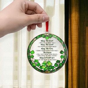 May include: Round ornament with a red ribbon, featuring a green and white design with shamrocks and the text "May The Road..." in a decorative font. The ornament has a stained glass effect.