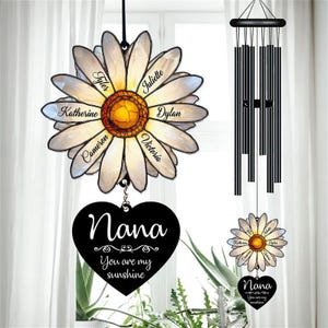 May include: A personalised daisy wind chime with names on the petals and a heart that says "Nana, You are my sunshine." The wind chime has a black top and chimes, and a smaller version of the daisy and heart.