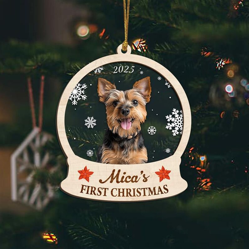 May include: Wooden Christmas ornament featuring a Yorkshire Terrier dog inside a snow globe design. The ornament includes the text "2025" and "Mica's FIRST CHRISTMAS". Decorative snowflakes and red star accents complete the design. The ornament hangs from a gold string.