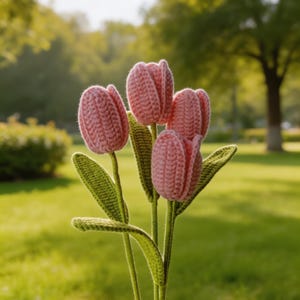 Könnte beinhalten: Ein Strauß aus vier gehäkelten Tulpen mit zartrosa Blütenblättern und einer strukturierten Garnoberfläche. Jede Blume ist an einem langen, schlanken grünen Stiel befestigt, mit spitzen grünen Blättern, die aus grünem Garn gefertigt wurden.