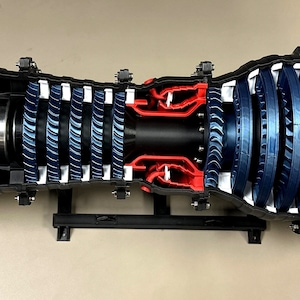 May include: A detailed cross-section model of a jet engine, showcasing internal components. The model features a black exterior with blue and red accents, including fan blades and internal structures. The engine is mounted on a black stand.