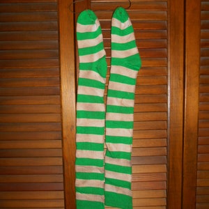 May include: A pair of green and white striped socks hanging on a wooden hanger.