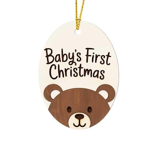 Peut inclure: Ornement de Noël ovale avec l'inscription "Baby's First Christmas" et un motif d'ours brun. L'ornement a un fond crème et une ficelle dorée. Une décoration festive pour le premier Noël d'un bébé.