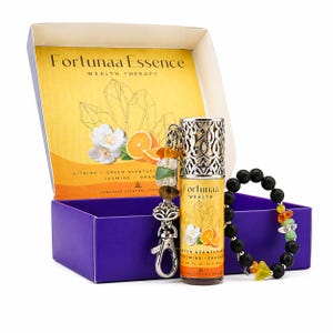 Puede incluir: Un juego de regalo que presenta un frasco de aceite esencial roll-on, una pulsera y un llavero con piedras preciosas. La botella está etiquetada como "Fortunaa Wealth" con imágenes florales y cítricas. El juego se presenta en una caja morada con interior amarillo.