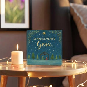 May include: A square, teal-colored Christmas card with the words "SEMPLICEMENTE Gesù" in gold script. The card features a nativity scene illustration and is next to a lit white candle. A string of lights is wrapped around the table.