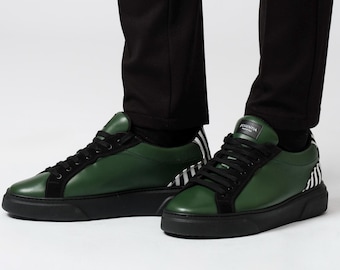 Puede incluir: Zapatillas de cuero verdes y negras con cordones y suelas negras. Las zapatillas tienen una puntera de ante negro y un diseño de rayas de cebra en el talón. El nombre de la marca "ESSENTIA" está impreso en la lengüeta.