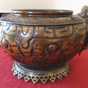 May include: A large, round, bronze incense burner with intricate carvings and a gold-coloured finish. The burner sits on a decorative, gold-coloured stand with a scalloped edge.