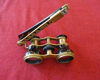 May include: Antique opera glasses with a gold-toned frame and black lenses. The handle is decorated with a tortoiseshell pattern. The glasses are set against a red background.