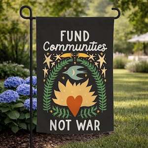 May include: Black garden flag with the text "FUND Communities NOT WAR" in white. The flag features a colorful design with a bird, stars, and a heart. The flag is displayed on a black metal stand in a garden setting.
