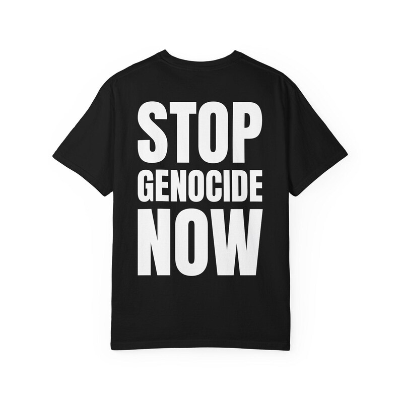 Op de afbeelding: Zwart t-shirt met de witte tekst "STOP GENOCIDE NOW" in grote letters. De tekst staat gecentreerd op de achterkant van het shirt. Het shirt heeft korte mouwen en een ronde hals.