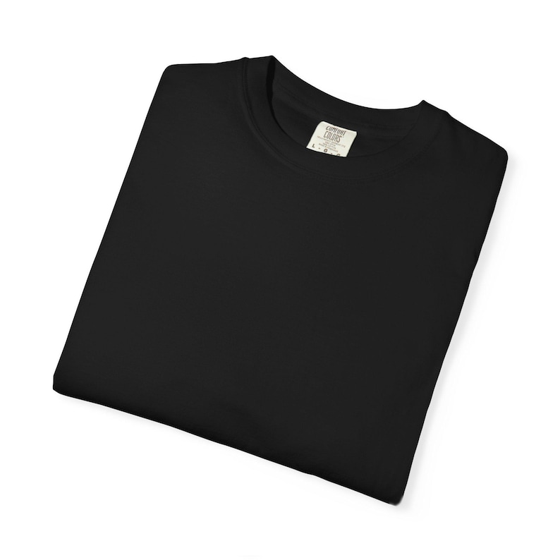 Op de afbeelding: Een gevouwen zwart t-shirt met een ronde hals. Het shirt heeft een label op de kraag met de woorden "COMFORT COLORS" erop gedrukt. Het shirt is gemaakt van een zacht materiaal en is netjes opgevouwen.