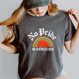 May include: Dark grey t-shirt featuring the text "No Pride In Genocide" in white gothic font above a rainbow and watermelon design. The shirt is a short-sleeved crew neck.