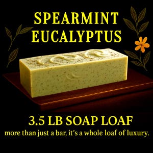 May include: A rectangular, light green soap loaf with the text "SPEARMINT EUCALYPTUS" and "3.5 LB SOAP LOAF". The soap has a textured surface and decorative swirls. The image is on a dark brown surface with a black background.