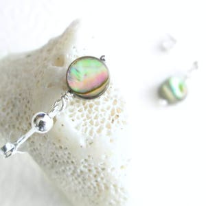 pink and green abalone shell earrings on sterling silver post, resting on a piece of coral