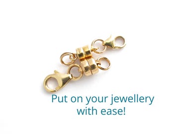 May include: Gold magnetic clasp for jewelry. The clasp is made of two round pieces of metal that connect with magnets. The clasp is attached to two gold chains with lobster claw clasps.