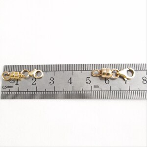 May include: A gold-toned magnetic clasp for a necklace or bracelet, measured against a ruler. The clasp is approximately 1 cm long.