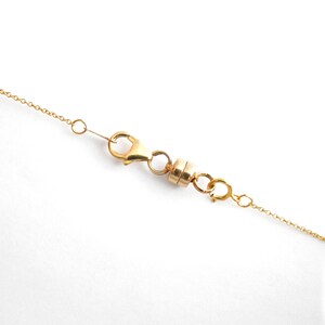 May include: Gold chain necklace with a magnetic clasp. The clasp is made of two small gold circles connected by a gold bar.