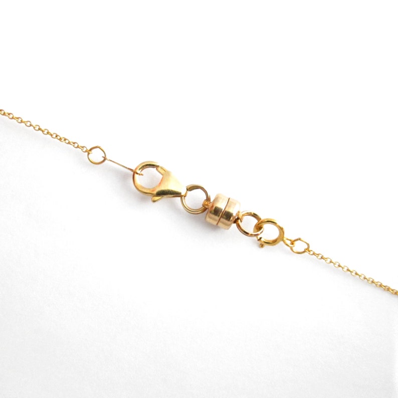 May include: Gold chain necklace with a magnetic clasp. The clasp is made of two small gold circles connected by a gold bar.