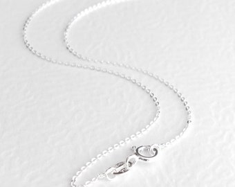 May include: A delicate silver chain necklace featuring a series of small, round, interconnected links. The chain includes a circular spring ring clasp mechanism at one end, designed to securely fasten the necklace when worn around the neck.