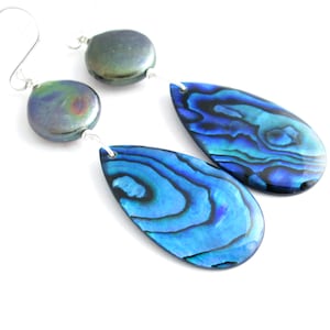 May include: A pair of dangle earrings featuring iridescent blue abalone shell teardrop pendants. The earrings also have dark gray, round beads and silver-tone ear wires. The abalone shells display a vibrant, swirling pattern of blues and greens.