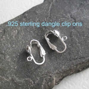 May include: Two silver .925 sterling dangle clip on earrings. The earrings are made of metal and have a small ball at the end of the dangle.