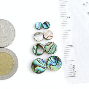 4 sets of round abalone shell beads in the available sizes of 6 mm, 8 mm, 10 mm and 12 mm next to an inch ruler, a US quarter and a 2 Euro coin. Blue, green, yellow and pink