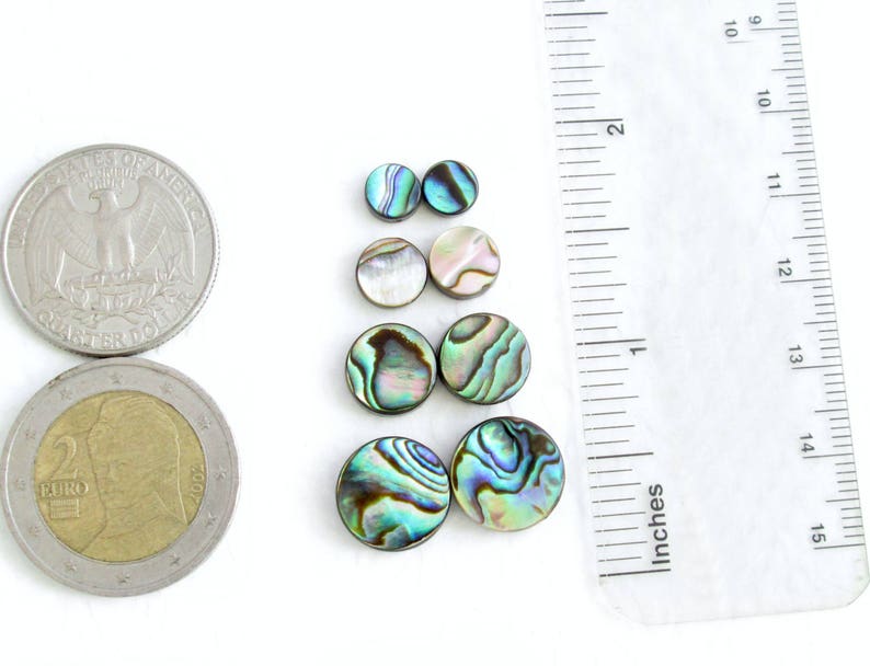 4 sets of round abalone shell beads in the available sizes of 6 mm, 8 mm, 10 mm and 12 mm next to an inch ruler, a US quarter and a 2 Euro coin. Blue, green, yellow and pink