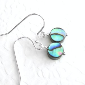 Könnte beinhalten: Ein Paar silberne Ohrringe mit runden Perlen aus irisierendem blauem und grünem Abalone-Muschelschalen.