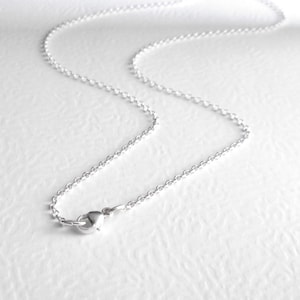 May include: A silver-coloured metal chain necklace featuring a series of small, uniform circular links. The necklace is secured with a small, rounded lobster claw clasp mechanism at one end, which connects to a small jump ring for closure.