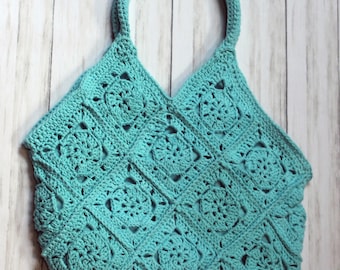 May include: A turquoise crochet tote bag with a floral pattern. The bag features a rounded handle and is constructed from square crochet motifs. The bag is made of a soft, textured yarn.