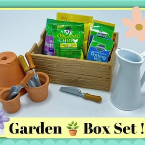 May include: A garden box set with a wooden crate filled with soil packets, terracotta pots, and gardening tools. Includes a white pitcher and the text "Garden Box Set!"