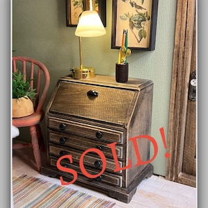 May include: Miniature wooden desk with four drawers and a slanted top. A small lamp with a gold base and a white shade sits on top. The word "SOLD!" is written in red across the front of the desk.